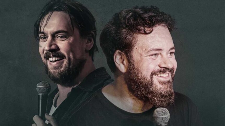 To komikere på scenen med mikrofoner, ler og smiler. Mørk bakgrunn. Stand-up underholdning.