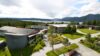 Utsikt over høyskolecampus ved fjord og fjellandskap i Norge, omgitt av skog under overskyet himmel.