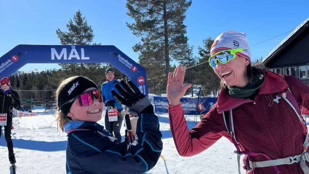 To skiløpere gir hverandre high-five ved målstreken i solfylt vær.