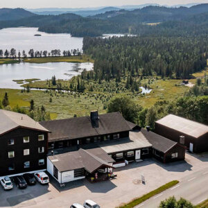 Panorama av hus ved innsjø omgitt av skog og fjell i et norsk landskap.