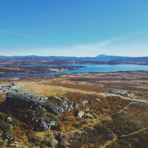 Utsikt over daler og innsjøer fra en høyde, med fjell i bakgrunnen på en klar høstdag.