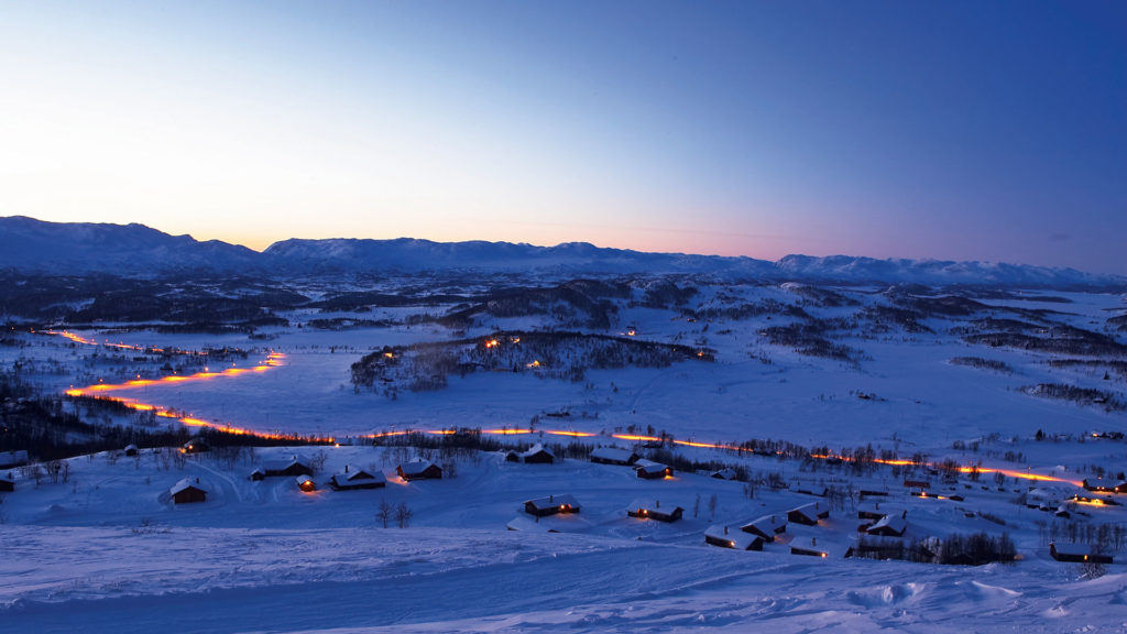 Landskap av vinterkveld i norske fjell med hyttebelysning og snøkledde omgivelser.