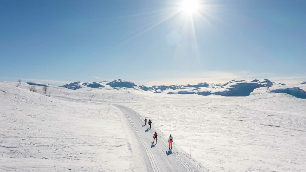 Tre skiløpere på langrenn i solfylt vinterlandskap med snødekte fjell i Norge.