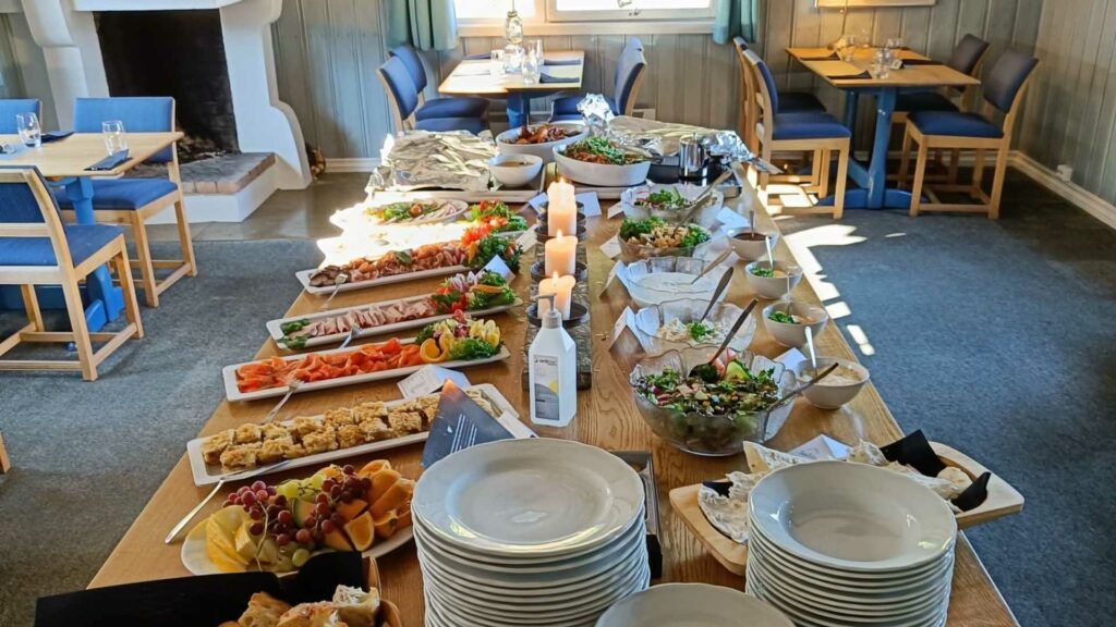 Buffet med et utvalg av salater, frukt, bakverk og kjøttretter på en lys trebord i en koselig spisestue.